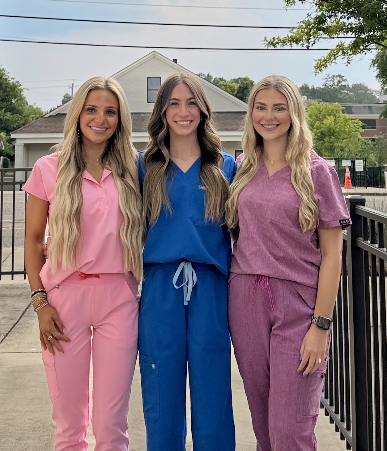 Three Shine Starkville estheticians in colorful scrubs smiling outside the studio